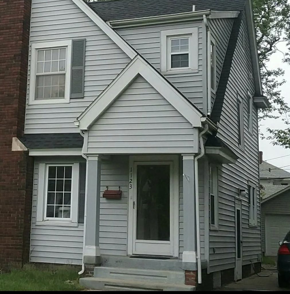 Exterior of a two-story home with gray siding, asphalt shingles, and gutters along the roofline, highlighting areas vulnerable to storm damage.